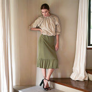 Woman in a moss green ruffle rib skirt with a beige top, showcasing a stylish, feminine look.
