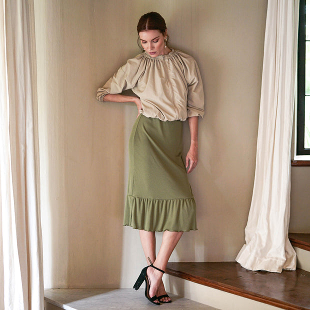 Woman in a moss green ruffle rib skirt with a beige top, showcasing a stylish, feminine look.