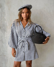 Model wearing the Meghan Mini Gingham Dress in Black with puff sleeves, styled with a matching beret and handbag.